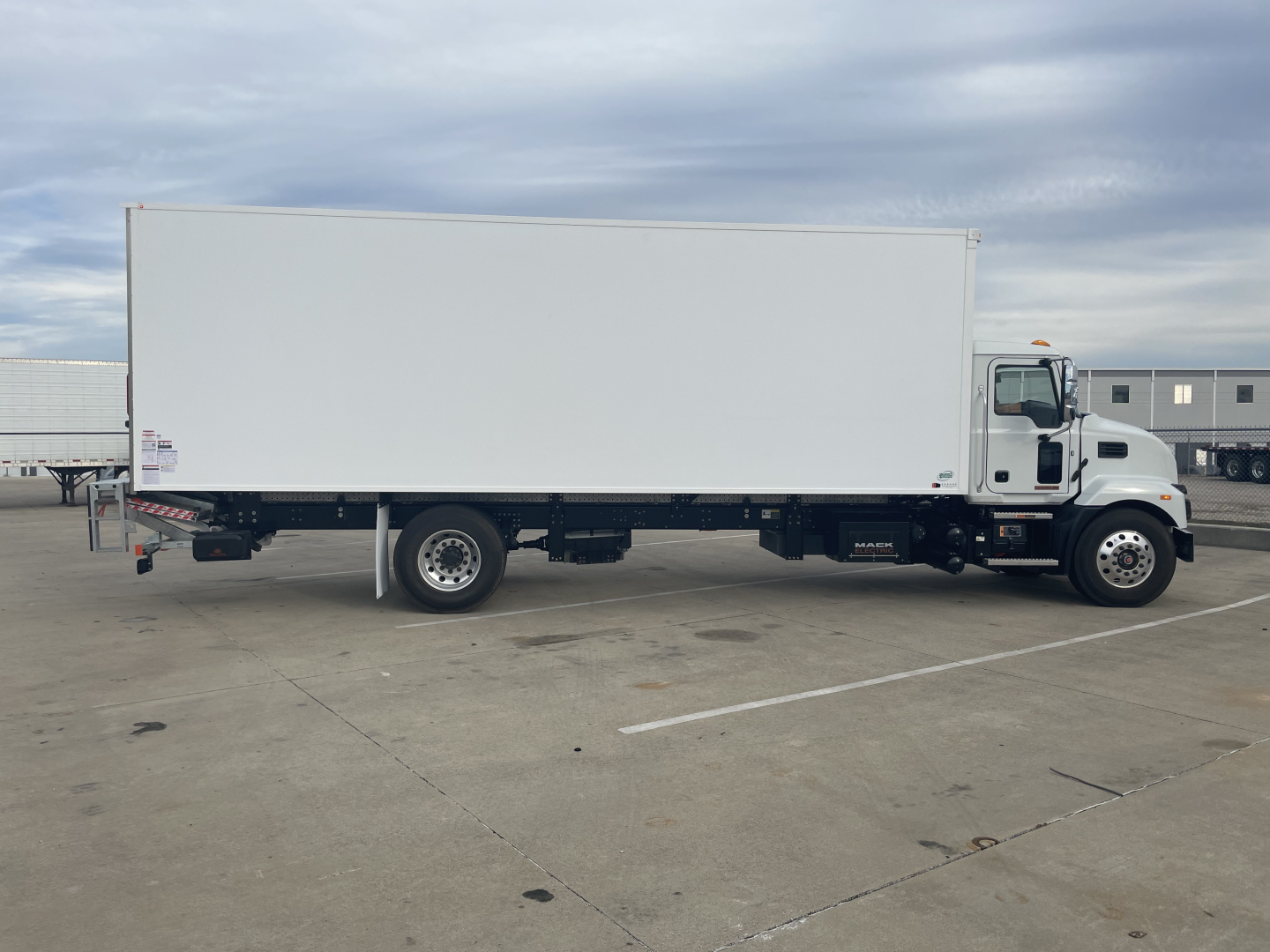 Box truck side view showing a white cargo box on a Mack MD6 chassis with black undercarriage and tires.