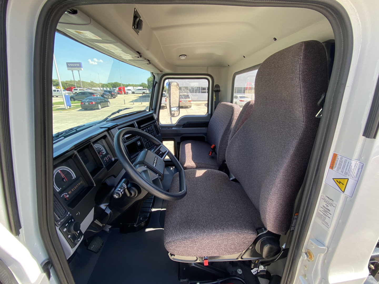 MD6 E truck cab interior showing steering wheel, driver seat, dashboard, and passenger seat with gray fabric upholstery.