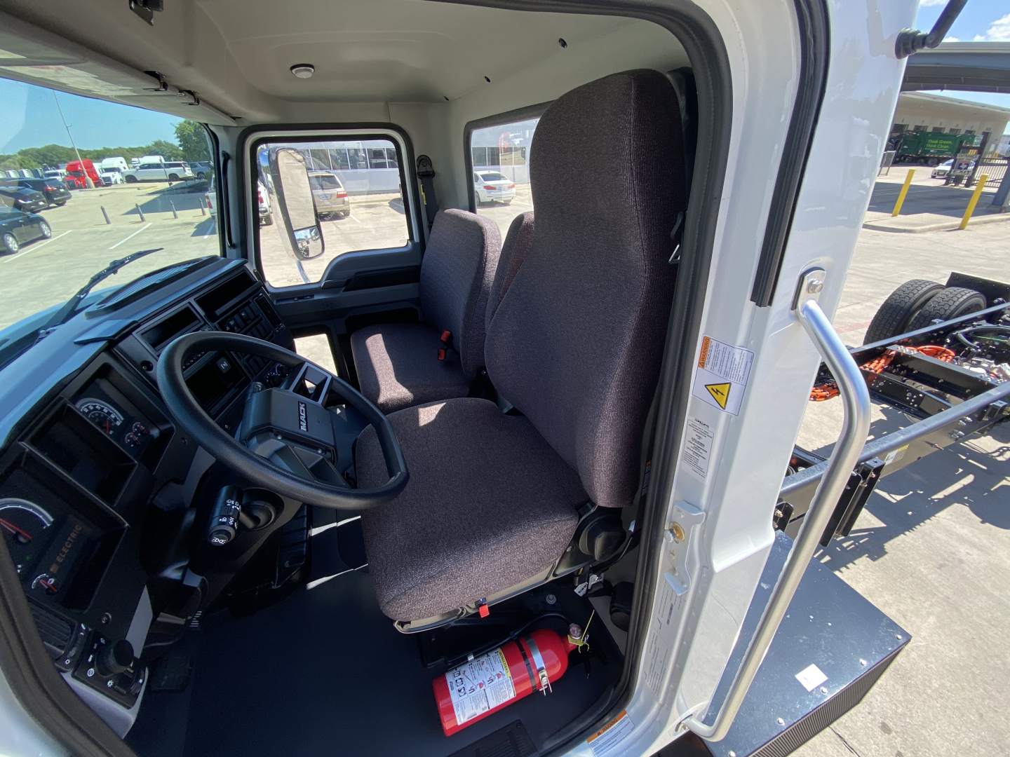 Cab interior of a 2024 Mack MD6 E truck showing front seats, steering wheel, dashboard, and a fire extinguisher in the cabin.