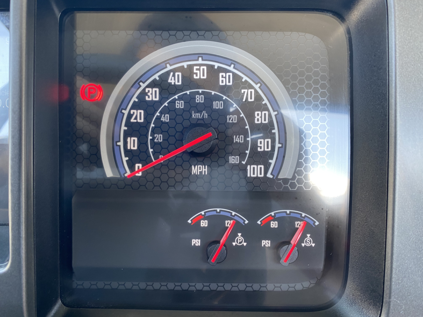 Dashboard view of a 2024 Mack MD6 E truck showing speedometer up to 100 mph, incl. red needle at idle, two small gauges with PSI measurements, and warning lights.