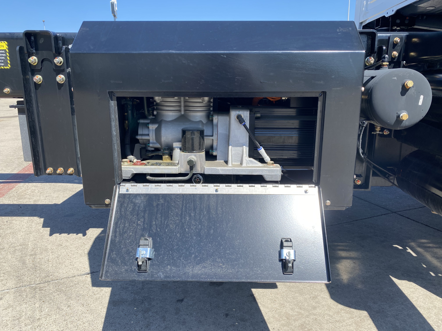 Mack MD6 E engine bay or equipment area showing exposed mechanical components and a metal drop-down access panel.