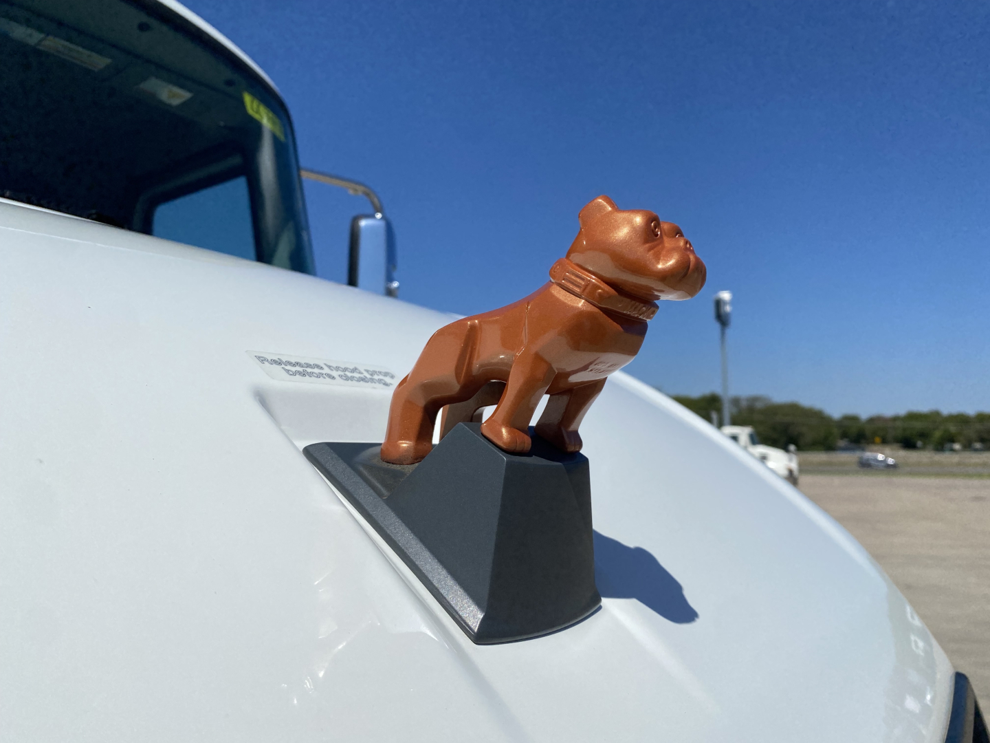 Tractor hood ornament dog figurine mounted on a Mack MD6 truck with blue sky background; visible badge text near hood shows powertrain details.