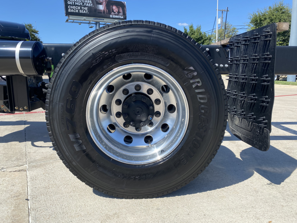 Truck wheel and tire close-up showing chrome wheel with lug nuts and spare wheel well; side of truck and mud flap visible.