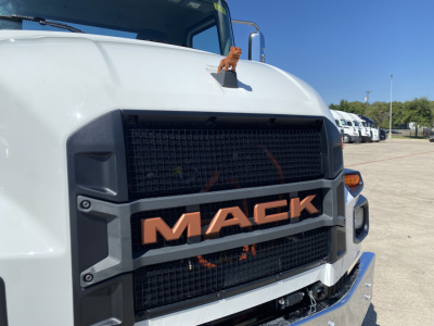 Mack truck MD6 front grille showing MACk lettering on grille and large black radiator, white cab, side mirrors, parking lot in background.