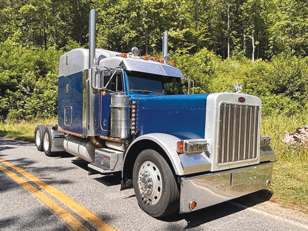 Peterbilt 379 UltraCab extended hood semi-truck in blue and chrome, front grille, dual exhaust stacks, large chrome bumper.