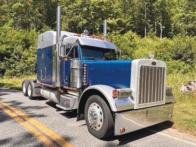 Peterbilt 379 UltraCab extended hood semi-truck in blue and chrome, front grille, dual exhaust stacks, large chrome bumper.
