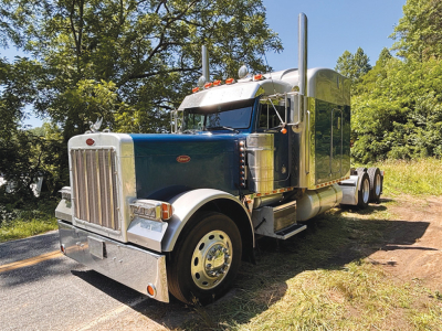 Peterbilt 379 UltraCab Extended Hood conventional truck in blue and chrome, front grille, dual exhaust stacks, side mirrors, daytime running lights, and sleeper cab area.