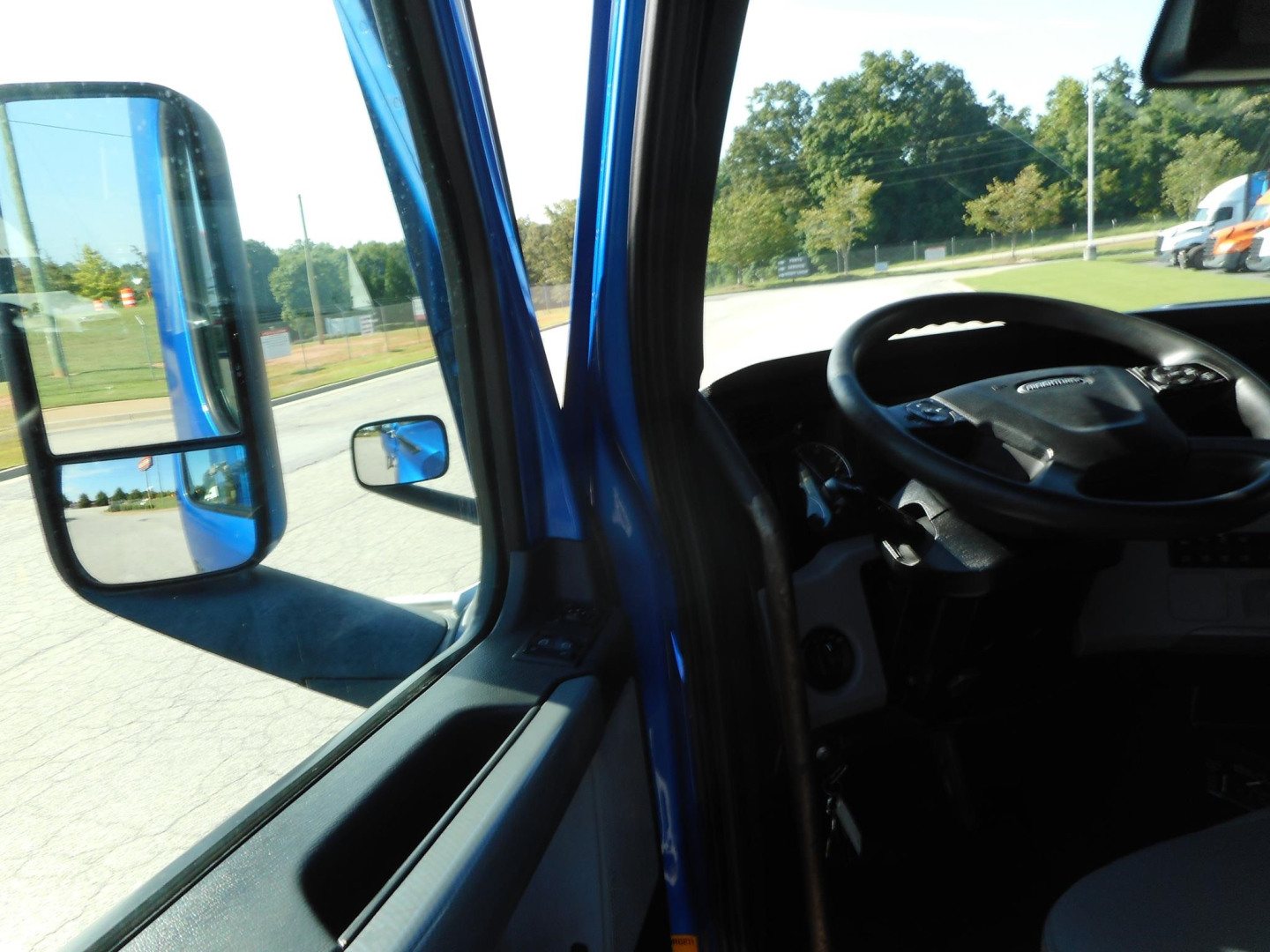 Truck cab interior and driver’s door area of a blue Freightliner Cascadia 126 showing steering wheel and dashboard from passenger side view.