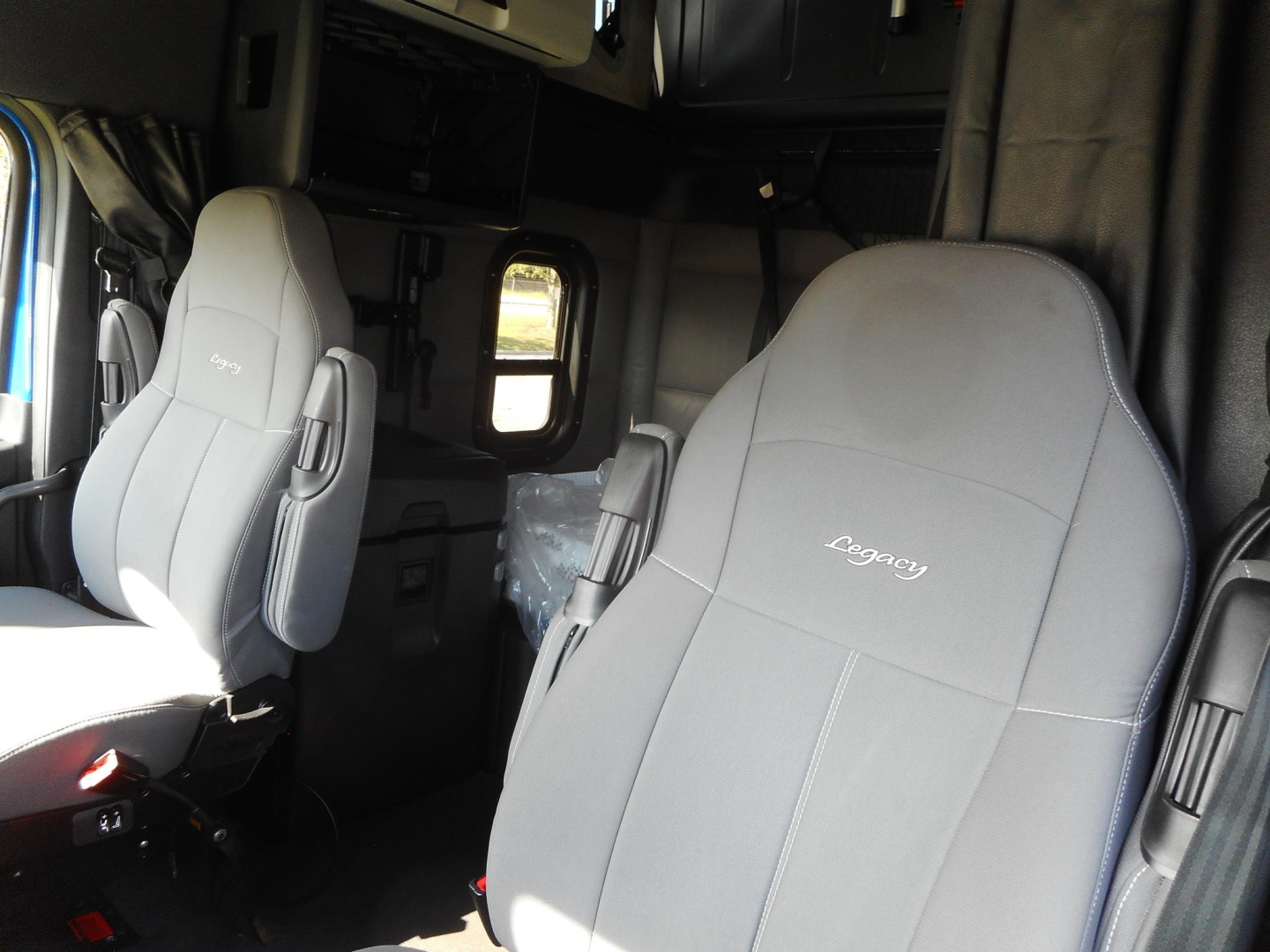 Cab interior of a 2022 Freightliner Cascadia 126 sleeper truck showing front seats with ‘Cascadia’ stitching and side window behind, part of the sleeper cabin.
