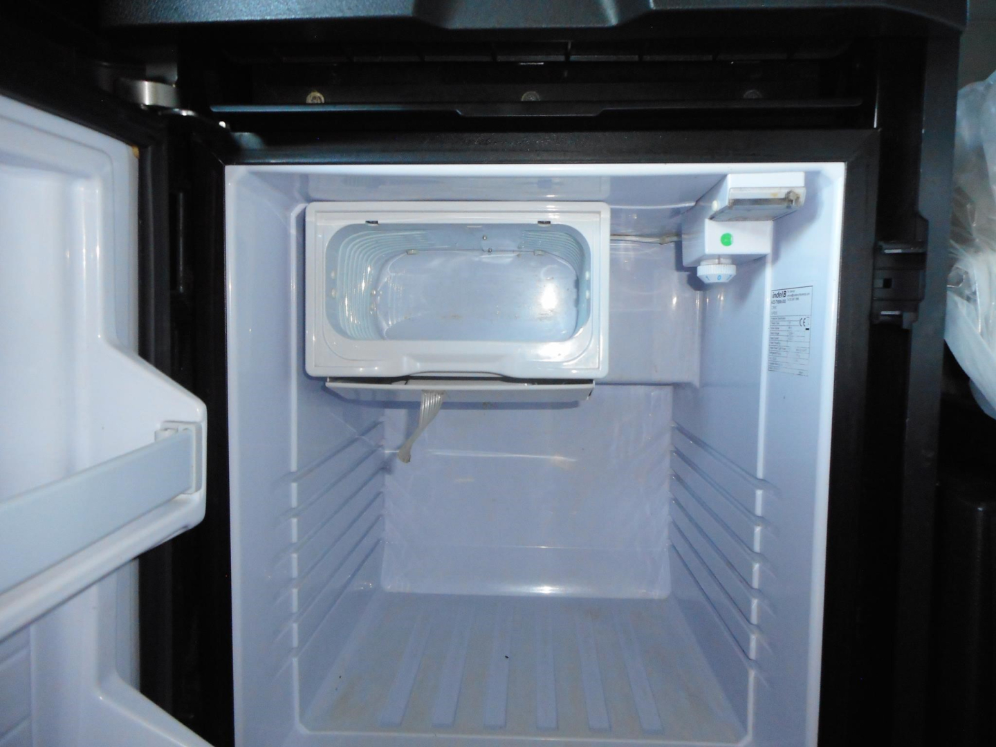 Freightliner Cascadia 126 engine bay showing empty freezer or storage compartment with light inside and small white control device on right wall.