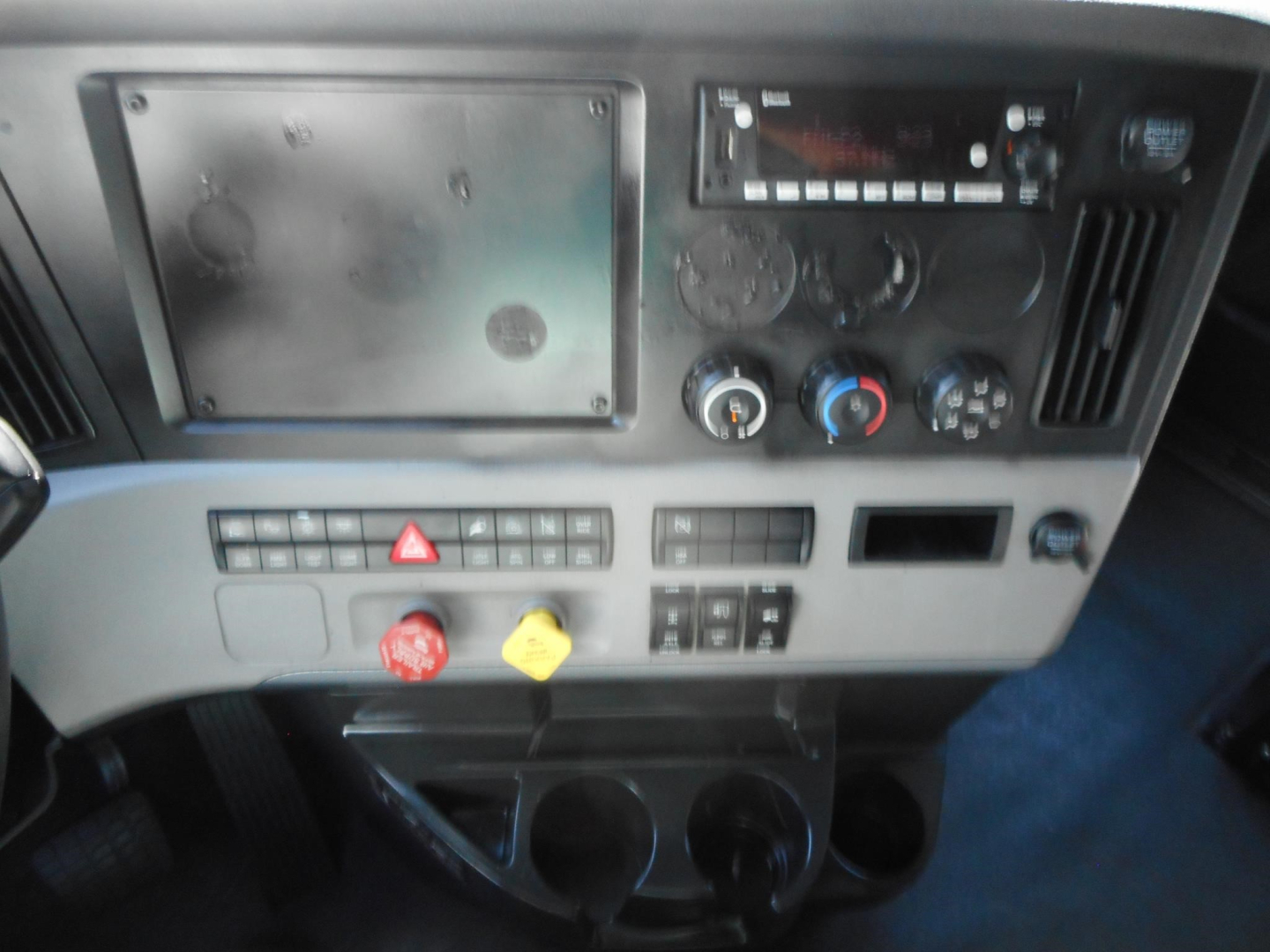 Dashboard panel of a Freightliner Cascadia 126 tractor showing climate controls and radio, with switches and cup holders.