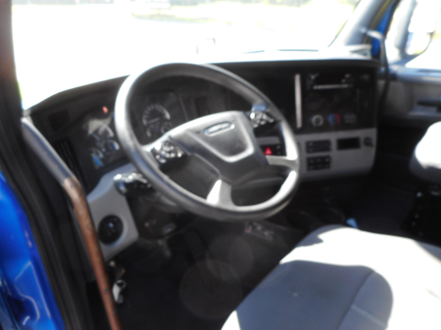 Freightliner Cascadia truck interior driver’s seat and dashboard view with steering wheel and instrument cluster visible.