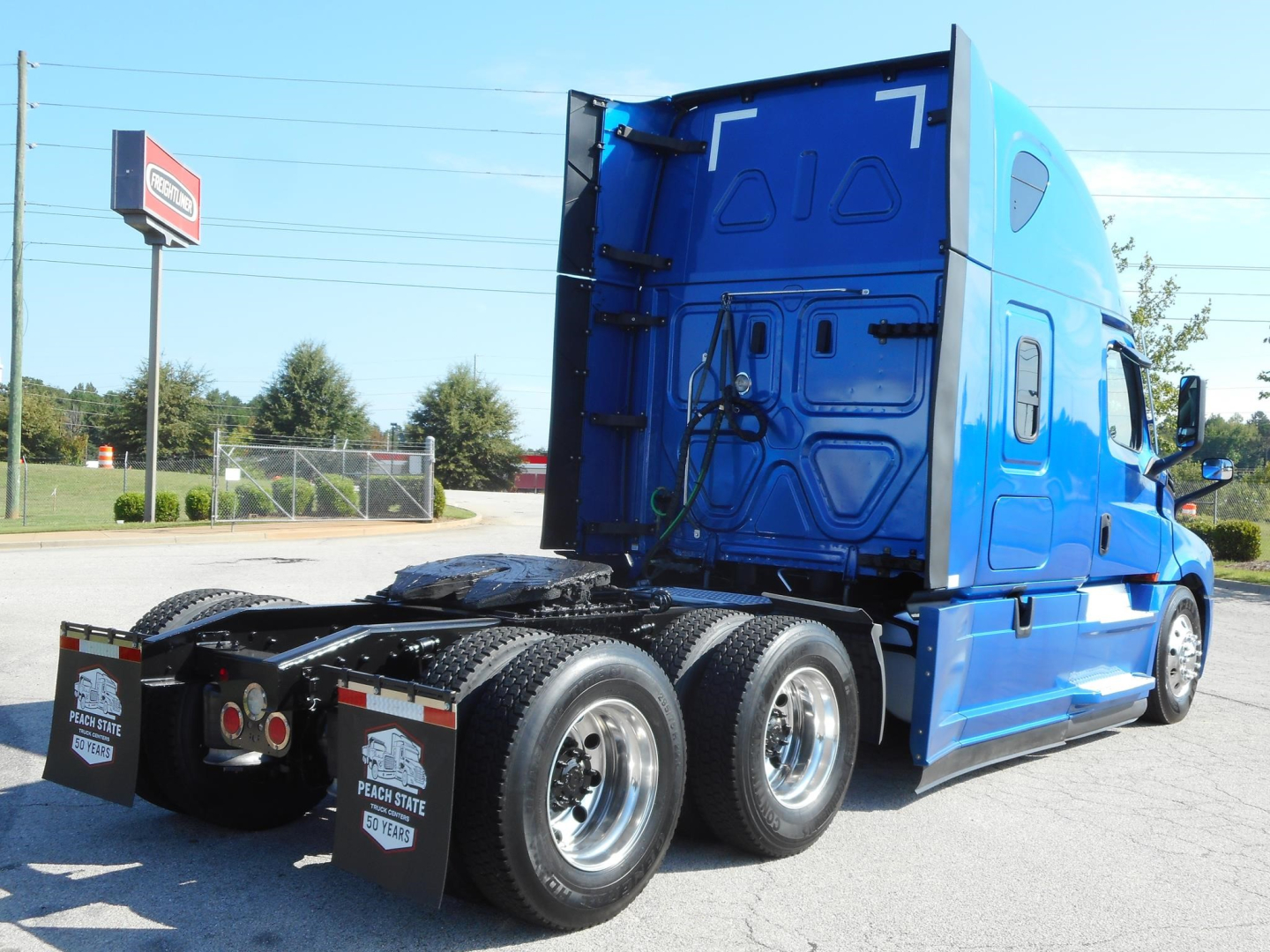 Blue Freightliner Cascadia 126 tractor-trailer, rear view showing fifth-wheel area and dual rear axles, daytime outdoor lot.