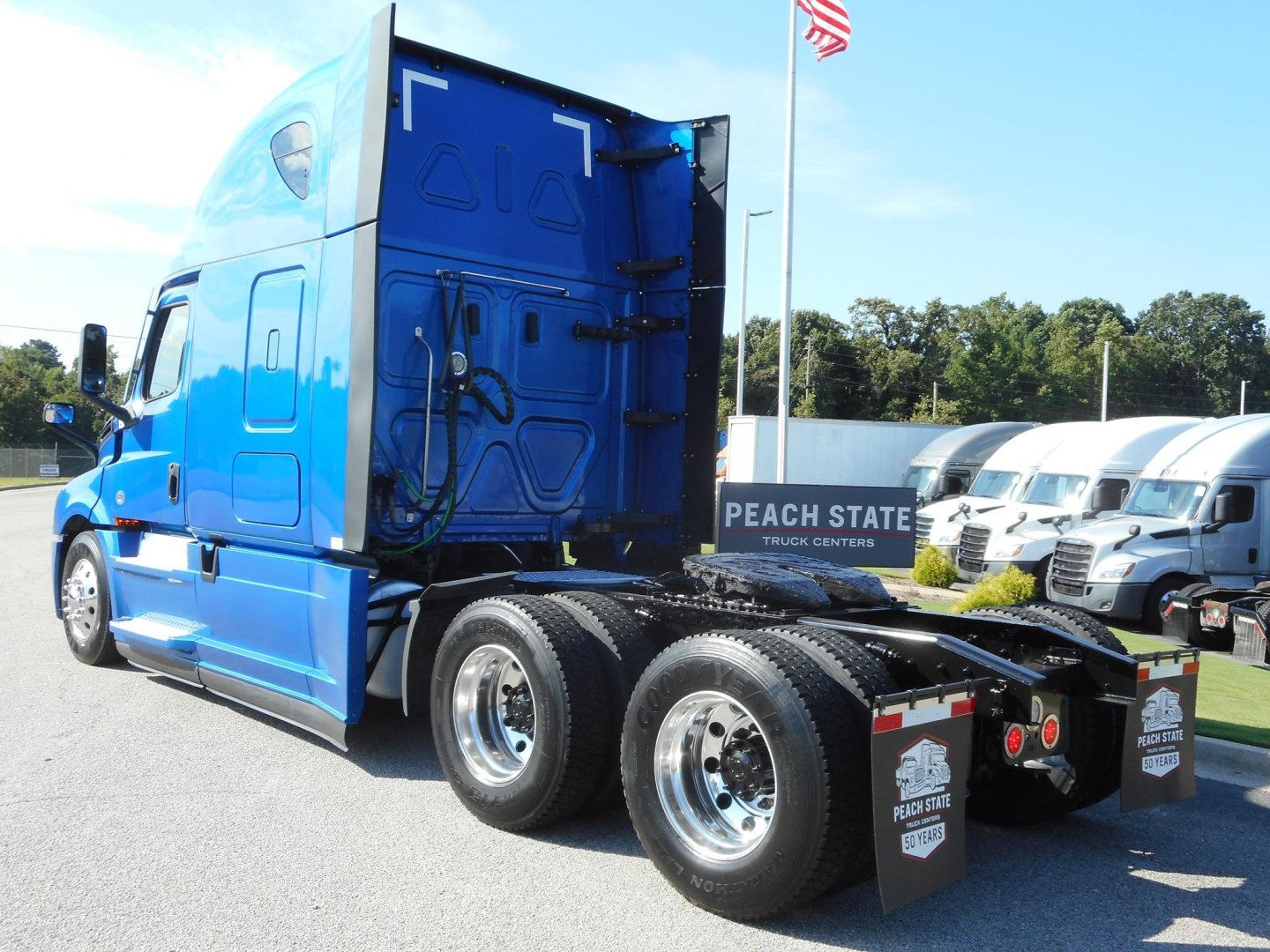 Freightliner Cascadia 126 truck in blue, rear view showing tractor’s fifth wheel, dual rear axles, and side fuel/air lines; Peachtree truck center sign in background.