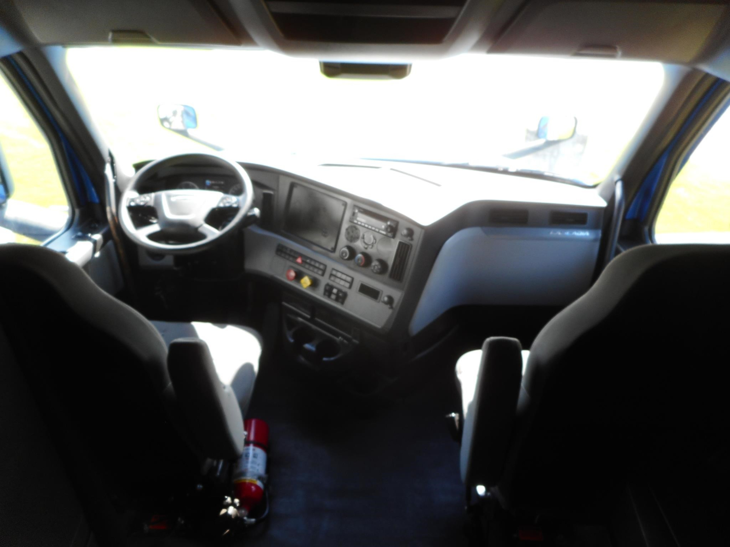 Interior of a Freightliner Cascadia truck cab showing the steering wheel, dashboard, and two front seats.