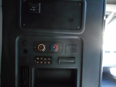 Cab interior panel of Freightliner Cascadia showing climate control dials, small electronic switch panel, and cubby storage area.