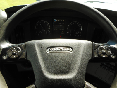 Cabin view of a Freightliner Cascadia steering wheel with instrument cluster and controls on both sides, center badge reads Freightliner.
