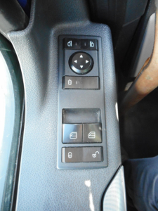 Control panel on driver door of Freightliner Cascadia showing mirror adjustment pad and window/lock switches.