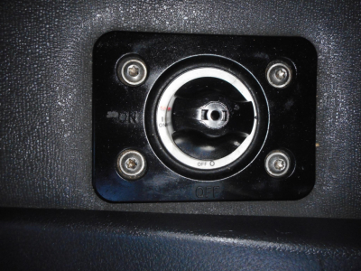 Cab interior view showing a circular ignition switch with a stainless ring and four screws in a black textured panel.