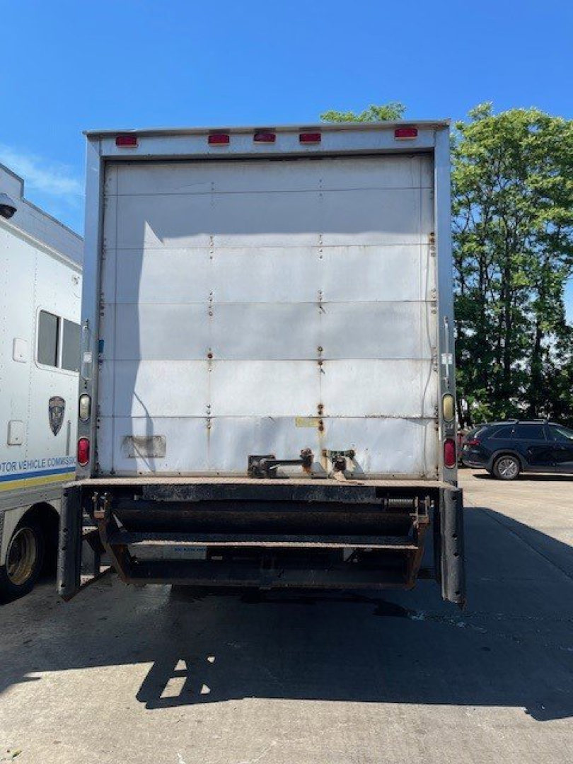 Interior rear view of a box truck tailgate and cargo area with metal panels and bumper. Visible rust spots, tail lights, and rear hitch area.