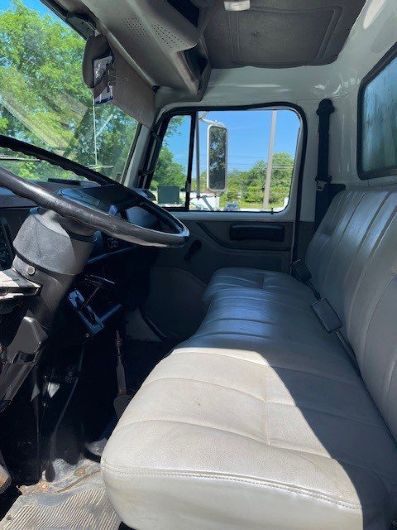 Interior cab view of a 1998 International 4000 Series truck showing gray bench seat, steering wheel, driver's door, and dashboard with large side window.