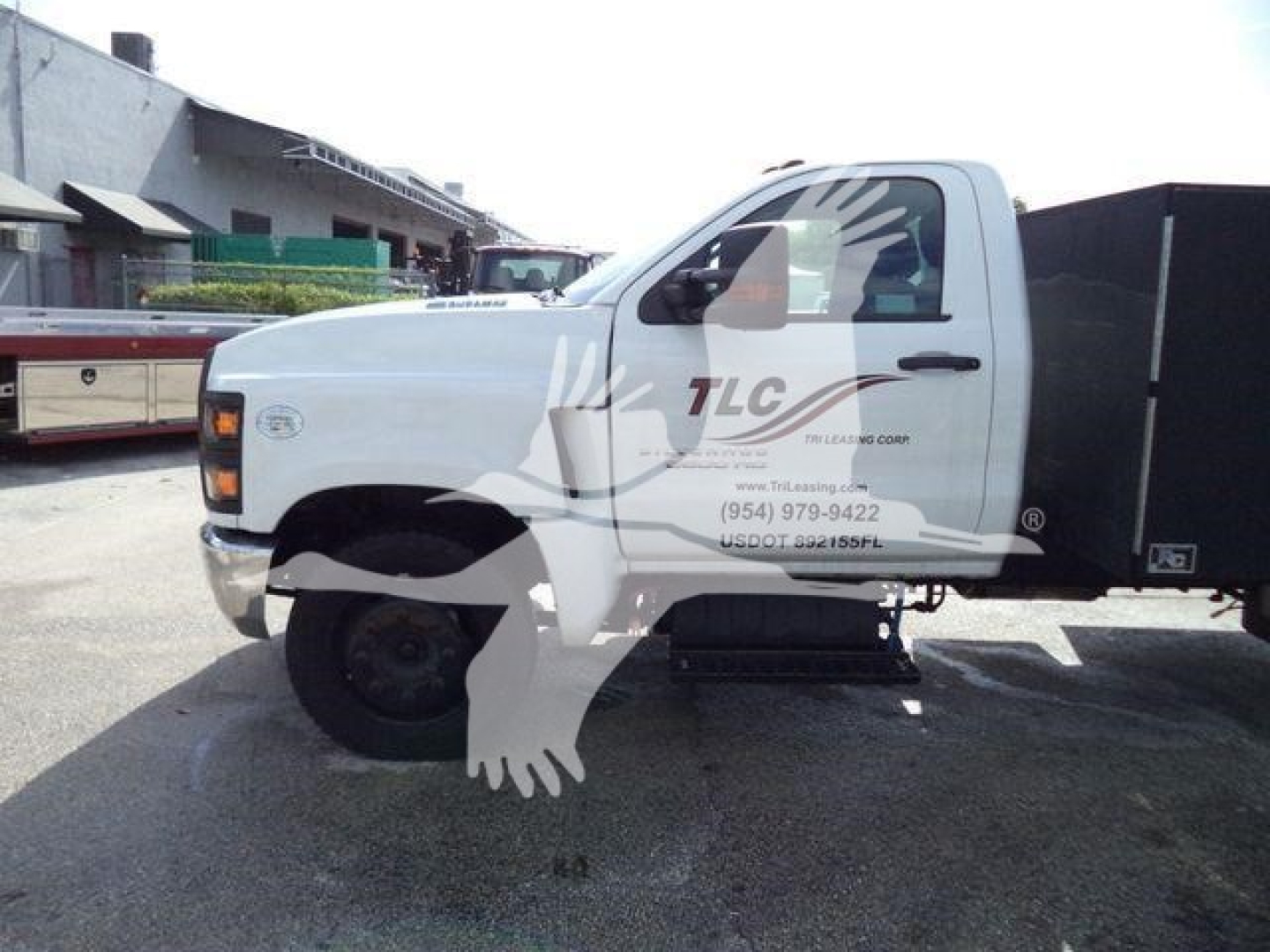 Chevrolet Silverado 6500HD service truck side view showing white cab with TLC logo and black dump bed in a lot.
