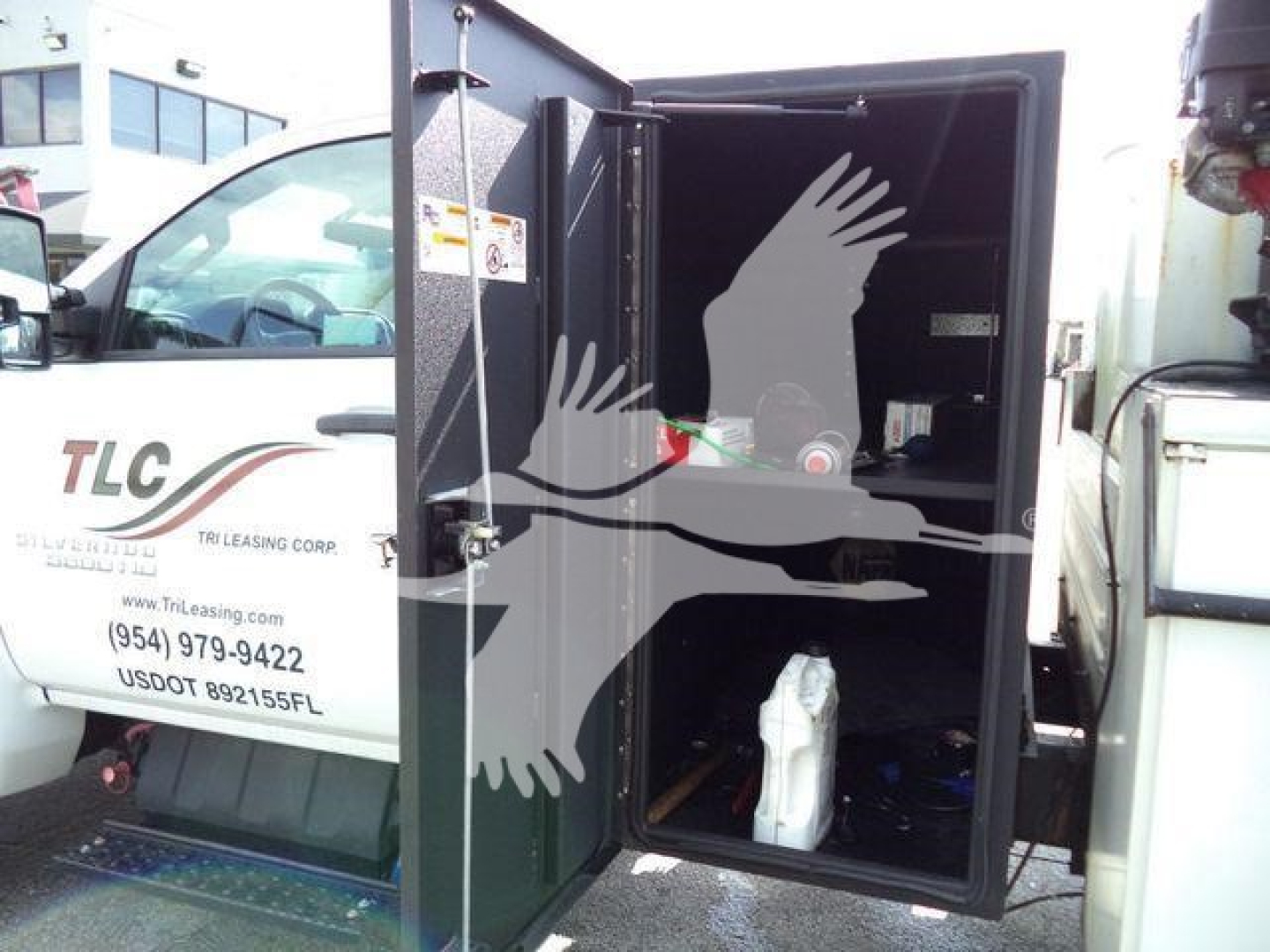 Utility truck rear compartment with open cargo area showing interior storage and a white container; side cab shows TLC Leasing Corp logo.