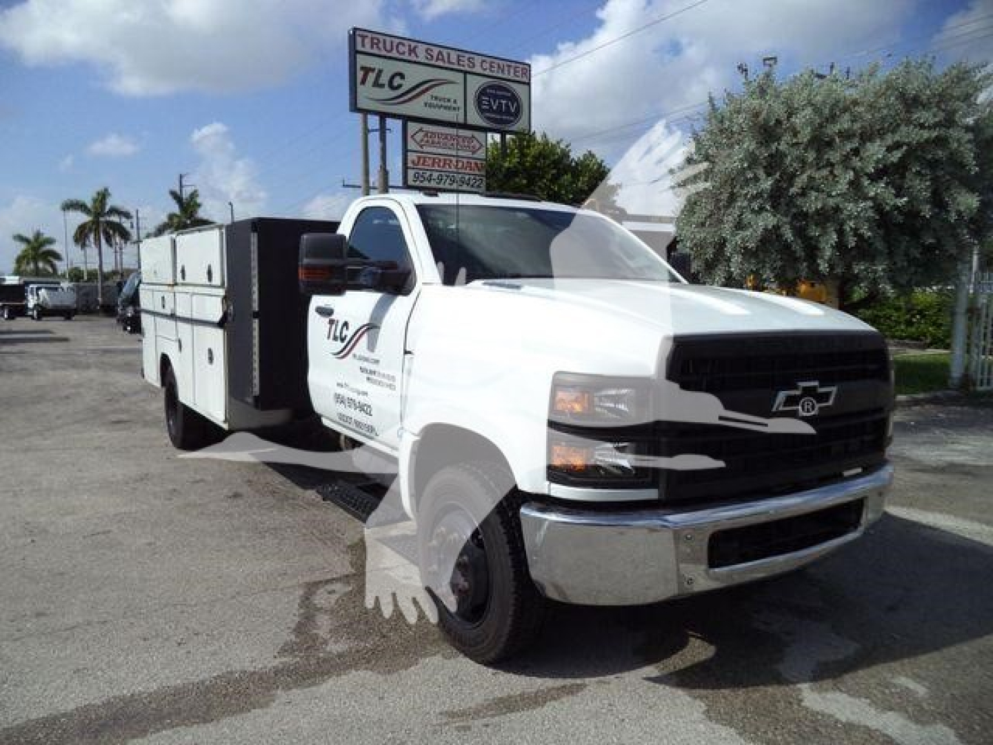 Truck with utility body showing TLC Truck Sales Center sign in background.