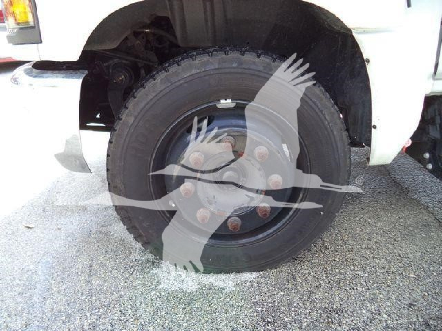Truck front wheel shown; tire and hub with lug nuts visible on a white Chevrolet Silverado 6500HD chassis, partial fender and suspension components in view.