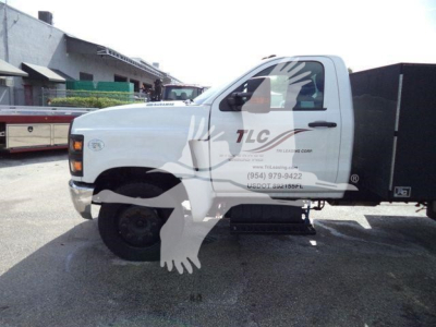 Chevrolet Silverado 6500HD service truck side view showing white cab with TLC logo and black dump bed in a lot.