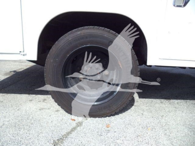 Vehicle wheel well and tire on a white service utility truck, partial fender visible