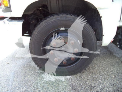 Truck front wheel shown; tire and hub with lug nuts visible on a white Chevrolet Silverado 6500HD chassis, partial fender and suspension components in view.