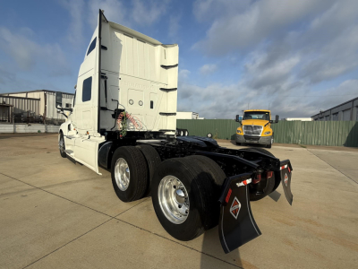 Semi truck tractor rear view with white cab and dual rear axles, fifth wheel in clean lot, other yellow truck in background.