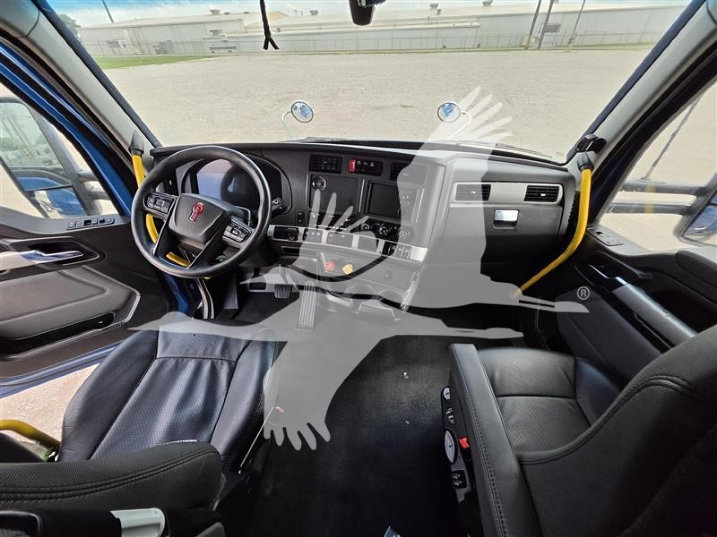 Kenworth truck interior cockpit view showing steering wheel with Kenworth badge, dashboard, center console, driver and passenger seats, and floor mat.