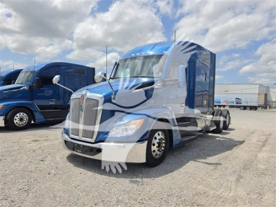 Kenworth T680 conventional sleeper truck in blue and white, front three-quarter view, with chrome bumper, large grille, and blue sky background.