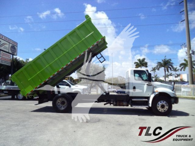 Dump truck with green dump bed raised in a parking lot, International MV model, side view, stock number T98791.