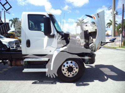 Truck cab with raised hood showing engine area and side steps; International MV dump truck in-service with white cab and exposed front end components.