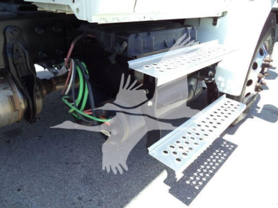 Truck step area showing undercab wiring, air hoses, and perforated metal steps attached to a cab-over section of a 2020 International MV dump truck.