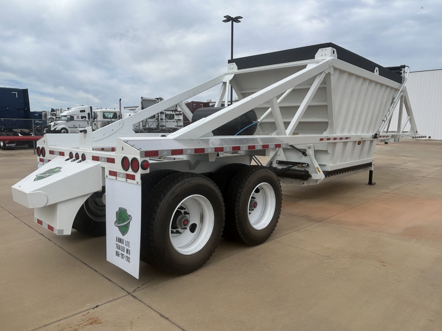 Trailer with white dump body and dual rear axles showing Armor Lite branding on rear mudflaps and reflective tape along sides; side railings and triangular support frame visible.
