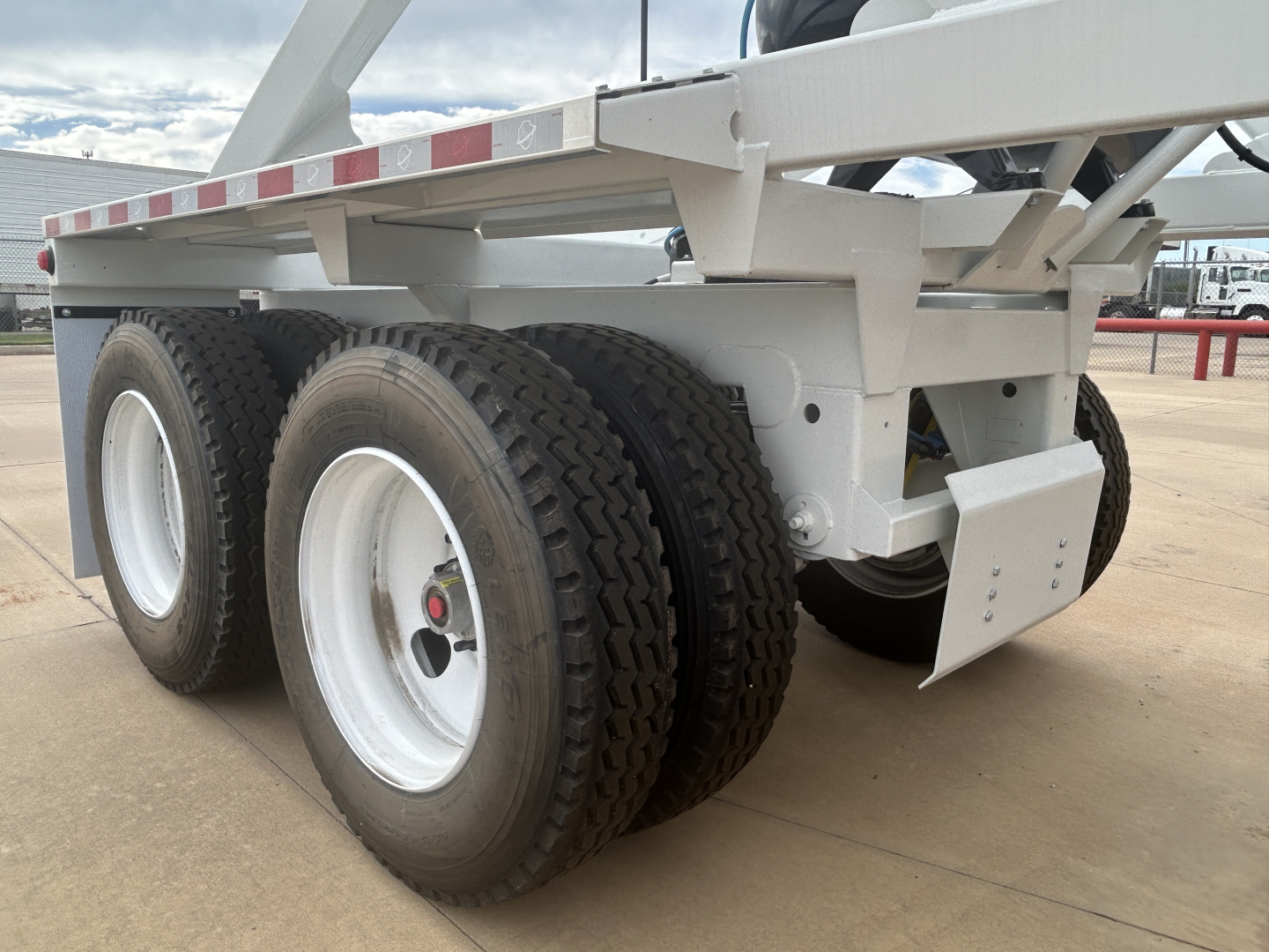 Trailer axle assembly showing two axles with dual tires and white rims, part of a gray Armor Lite SBD40 skeleton dump trailer.