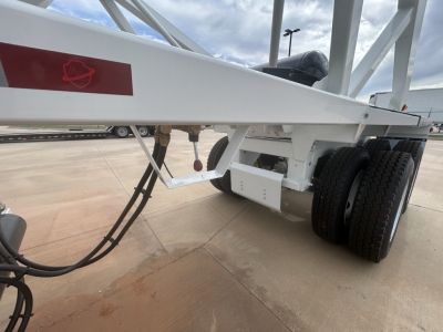 Dump trailer chassis with dual rear axles and white frame showing hydraulic lines and red safety marking.
