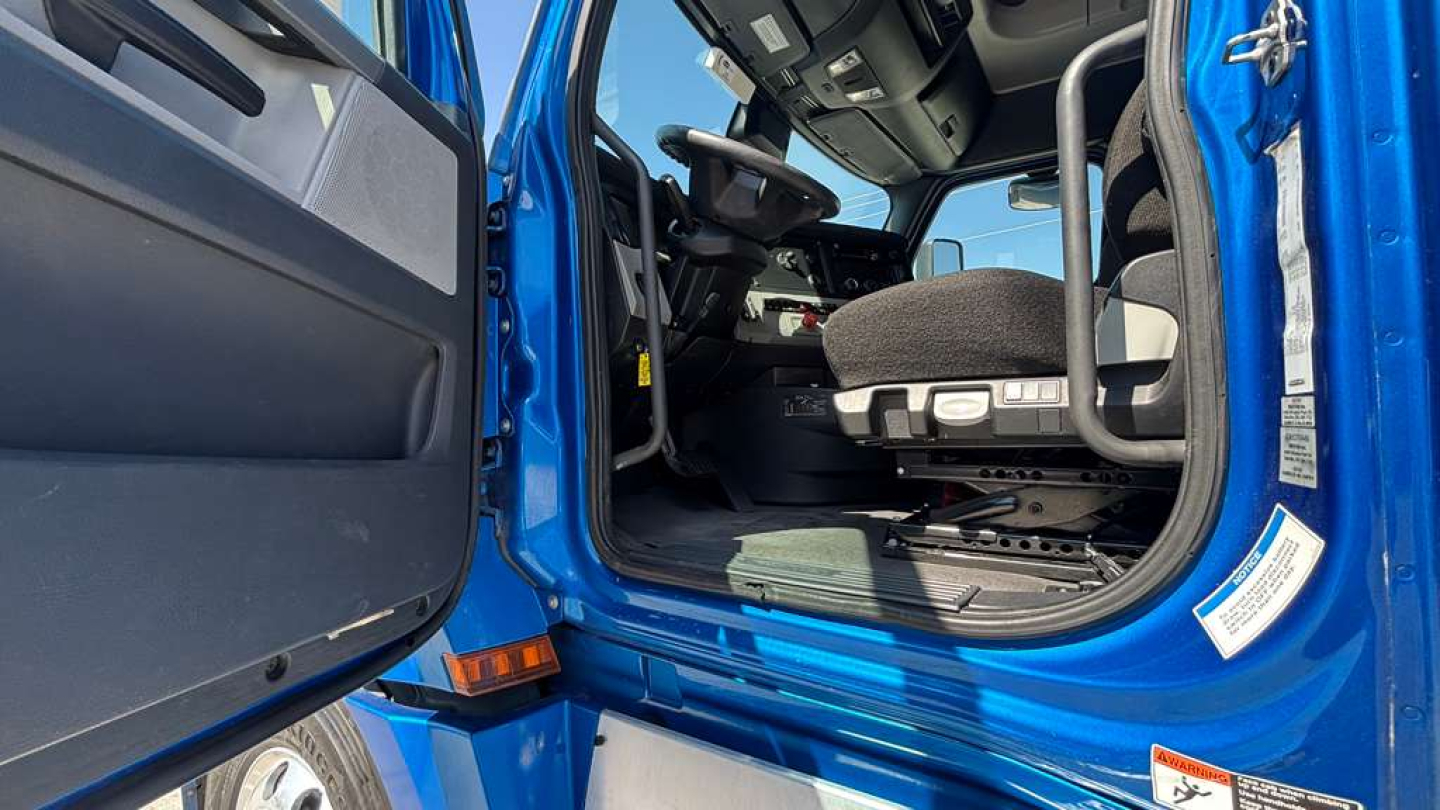 Truck cab interior viewed from doorway with driver's seat and dashboard; blue exterior paint visible on door frame and step area.