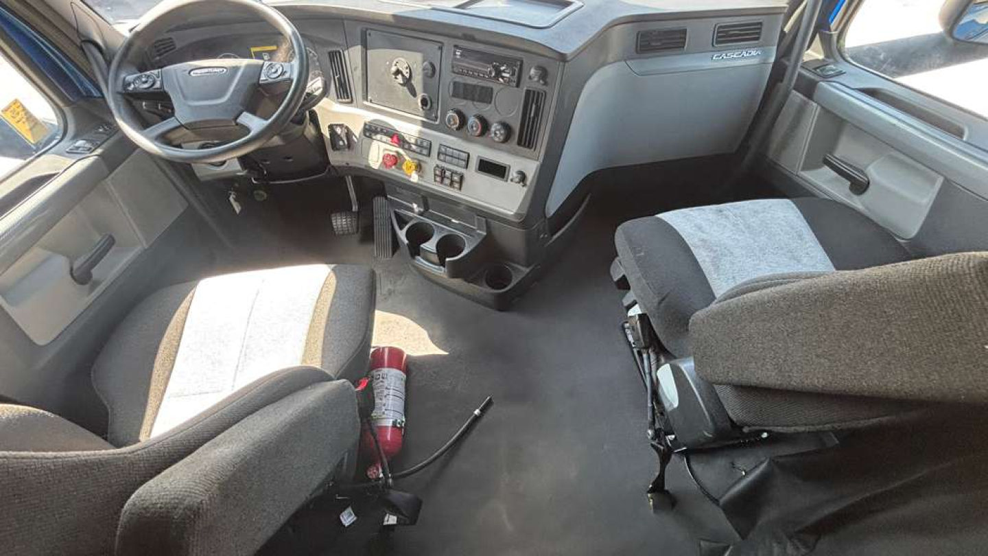 Cab interior of a 2022 Freightliner PT126064ST showing steering wheel, dashboard with controls, center console, and two seats with a fire extinguisher on the floor.