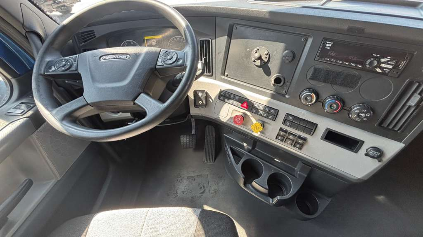 Cab interior of a Freightliner PT126064ST showing steering wheel, dashboard with gauges, controls, and cup holders.