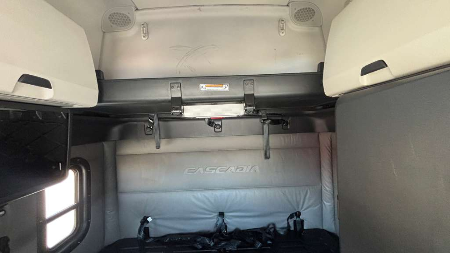 Cab interior of a Freightliner tractor showing storage compartments, sleeper area, and a light gray fabric cover with 'FLOGEN' text? (text may be 'EAGARA' unclear).