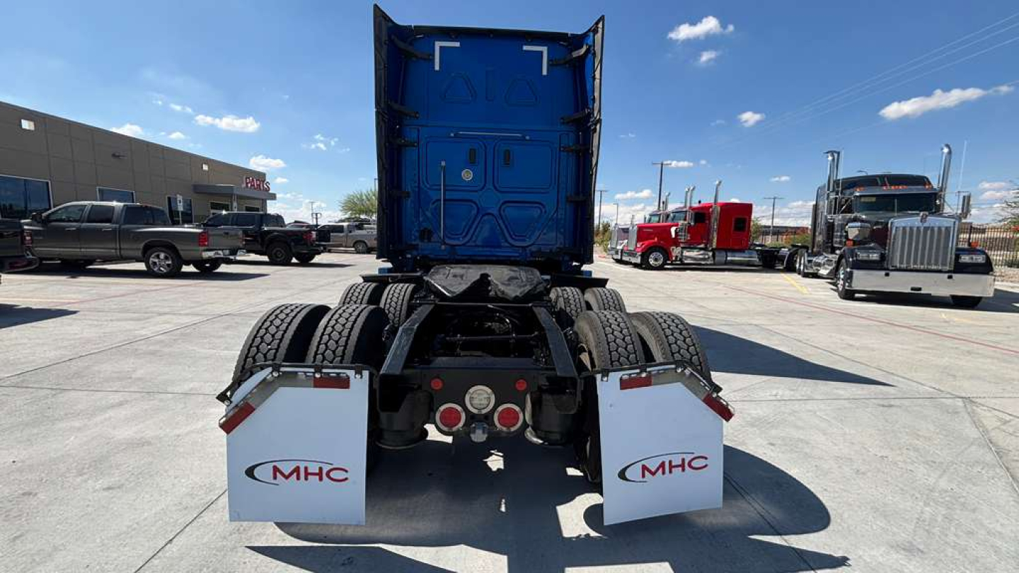 Rear view of a Freightliner semi-truck tractor with blue cab, dual rear wheels, and white MHC mud flaps.