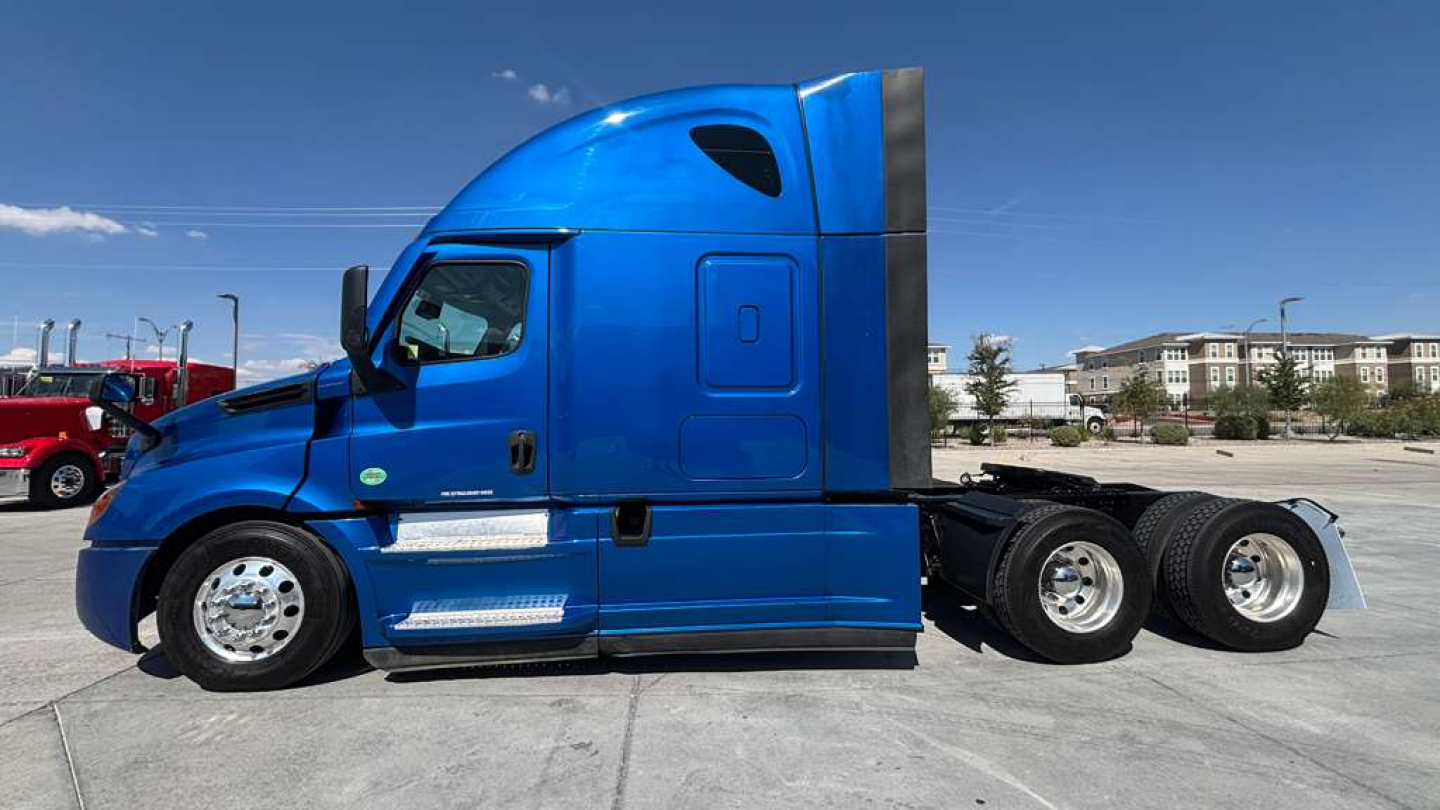 Truck side view of a blue Freightliner semi-truck tractor with sleeper, three axles, chrome fuel tanks, and silver rims.