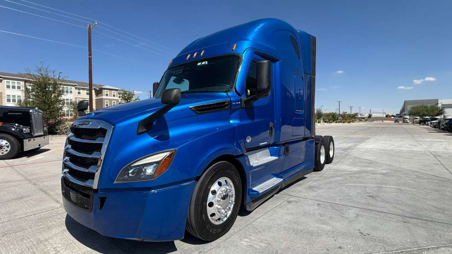 Truck cab showing blue Freightliner PT126064ST with Sleeper, side view, front grille, and dual rear wheels.