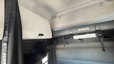 Truck cab interior view showing Euro-style sleeper van area with storage compartment and fabric headliner; partial Cascadia badge visible on panel.