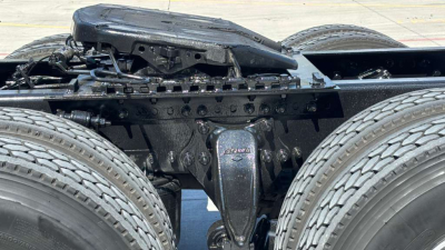 Tractor-trailer truck chassis with fifth wheel and dual rear axles, visible are frame rails, suspension, and drive components.